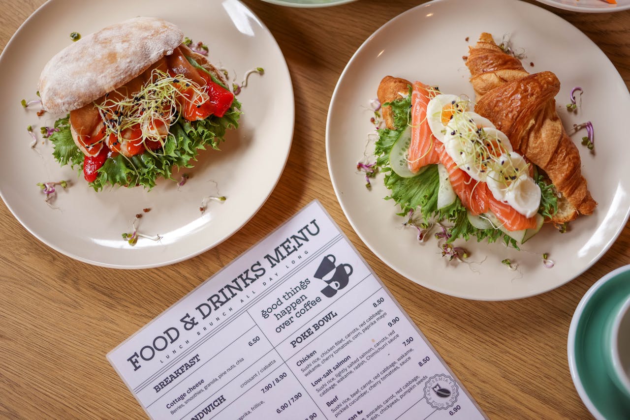 Top view of delicious salmon croissant and sandwich with fresh ingredients on wooden table.